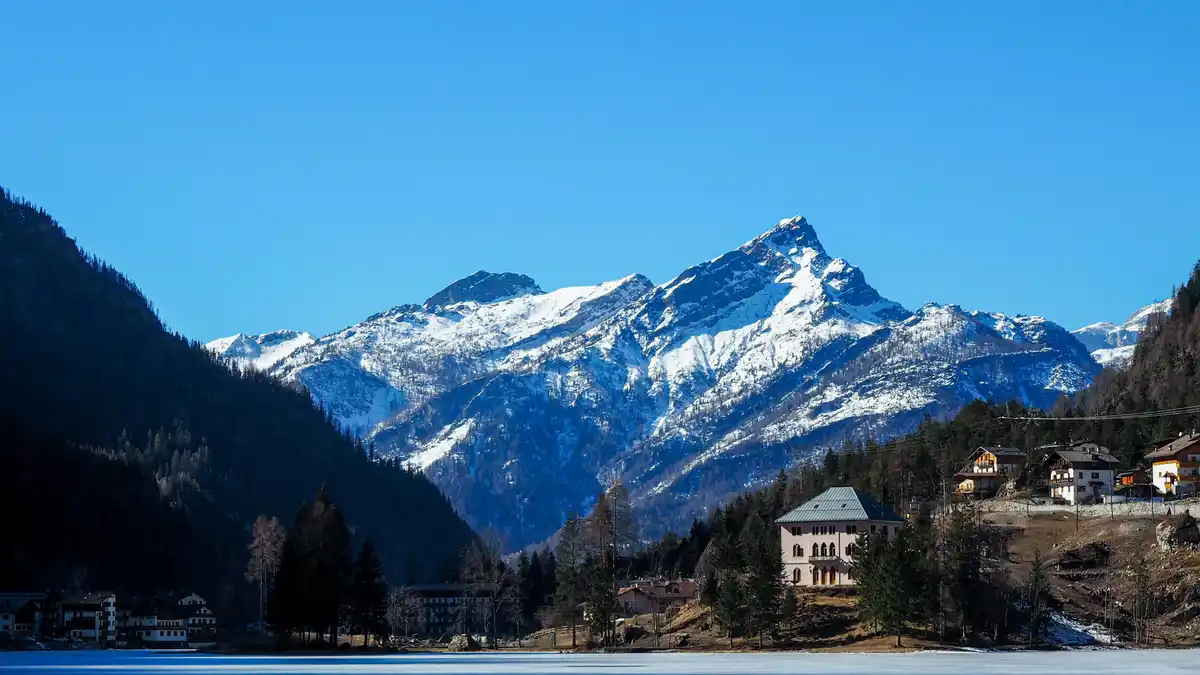Frosted peaks rise majestically above the lake's glassy surface, their snow-kissed crowns mirrored in the water's icy veil…