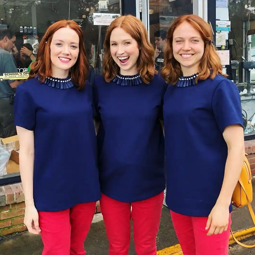 Three women with identical red hair and matching outfits — navy blue short-sleeved shirts with a ruffled collar and bright…