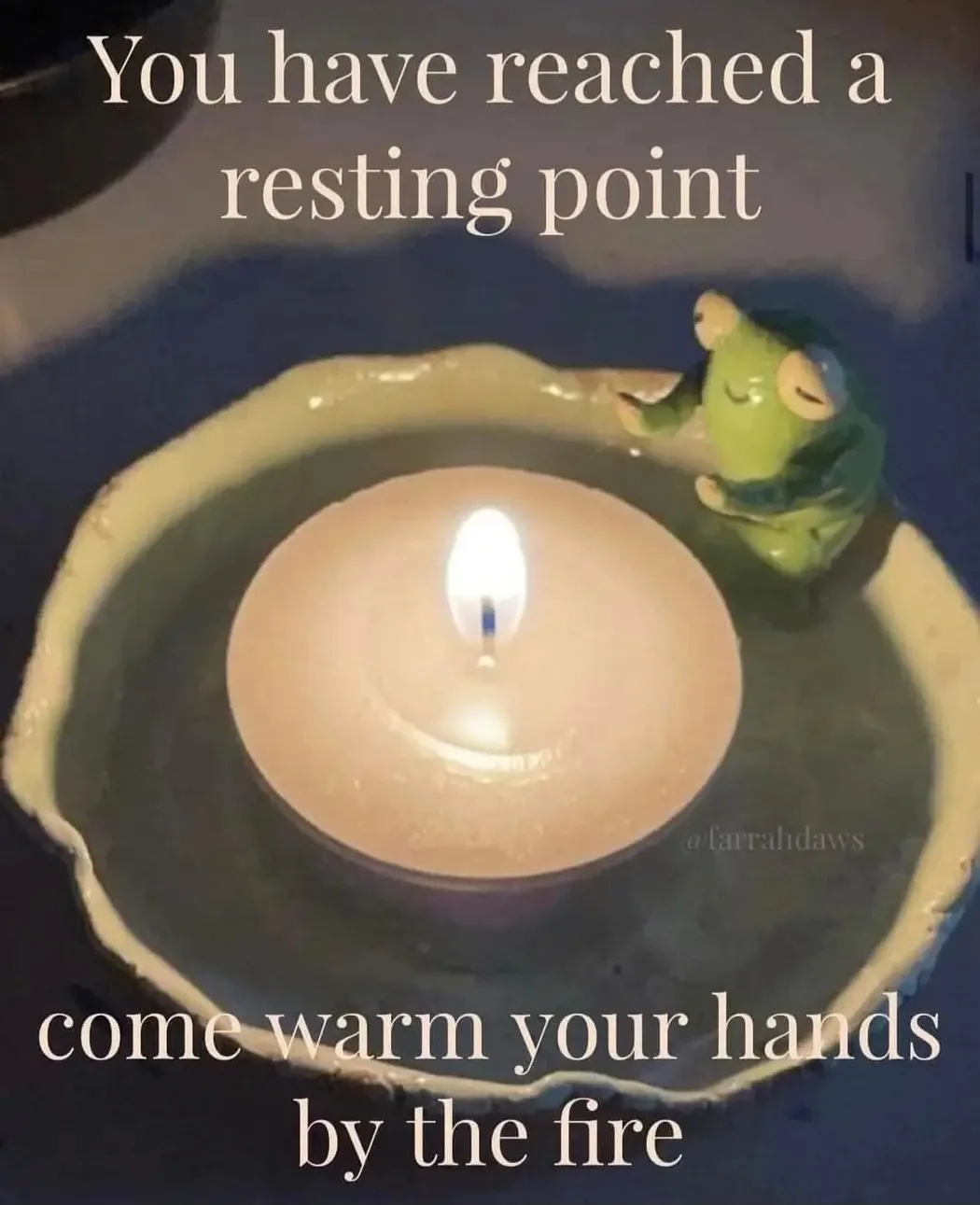 A lit tea light candle sits in a ceramic dish, with a small green frog figurine sitting beside it. White text overlaid at…