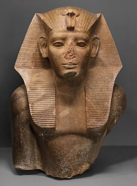 A stone bust of an ancient Egyptian pharaoh wearing a traditional nemes headdress with a uraeus cobra emblem on the…
