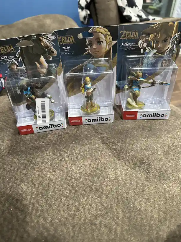 Three sealed Nintendo amiibo figures from The Legend of Zelda: Breath of the Wild are displayed side-by-side on a textured…