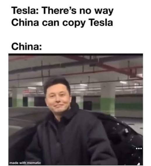 The image shows a man, identified as Elon Musk, smiling while sitting in the driver's seat of a black car in an underground…