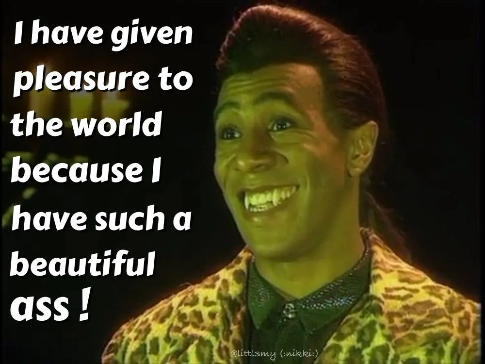 A man with a wide, toothy grin and styled hair wears a leopard-print jacket over a dark shirt. White text overlaid on the…