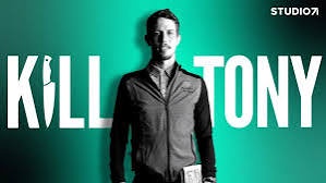 A man in a dark jacket stands against a green gradient background with the words 'KILL TONY' in large white letters across…