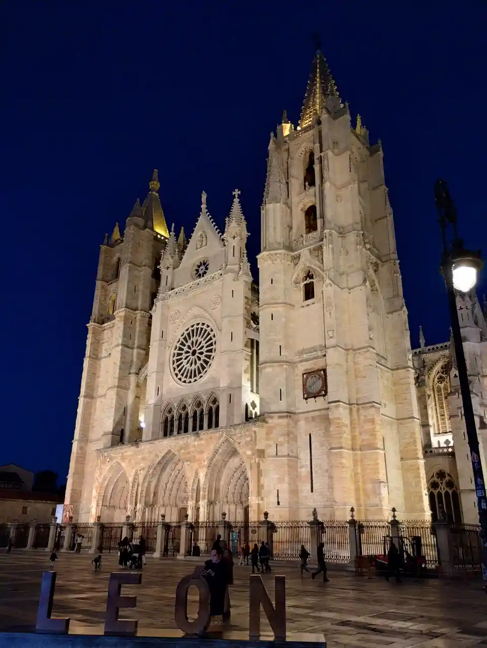 A nighttime photo of the illuminated Leon Cathedral in Spain, featuring its Gothic architecture, spires, rose window, and…