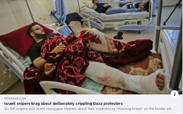 A man with a heavily bandaged leg lies in a hospital bed, covered by a red patterned blanket, in a room with other hospital…
