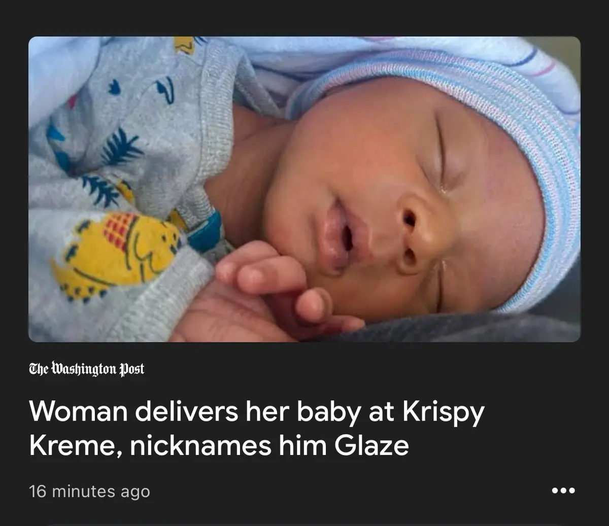 A close-up photo of a sleeping newborn baby wearing a blue striped hat and a grey onesie with a yellow cartoon character…