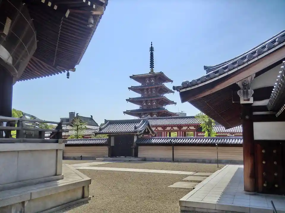 A photograph of a traditional Japanese temple courtyard with a multi-tiered pagoda in the distance, framed by the eaves of…
