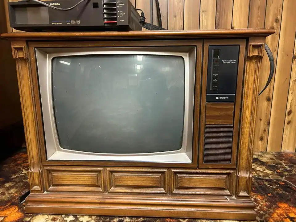 A vintage Hitachi CRT television with a wooden cabinet sits on a patterned rug, its screen dark and reflective, with a…