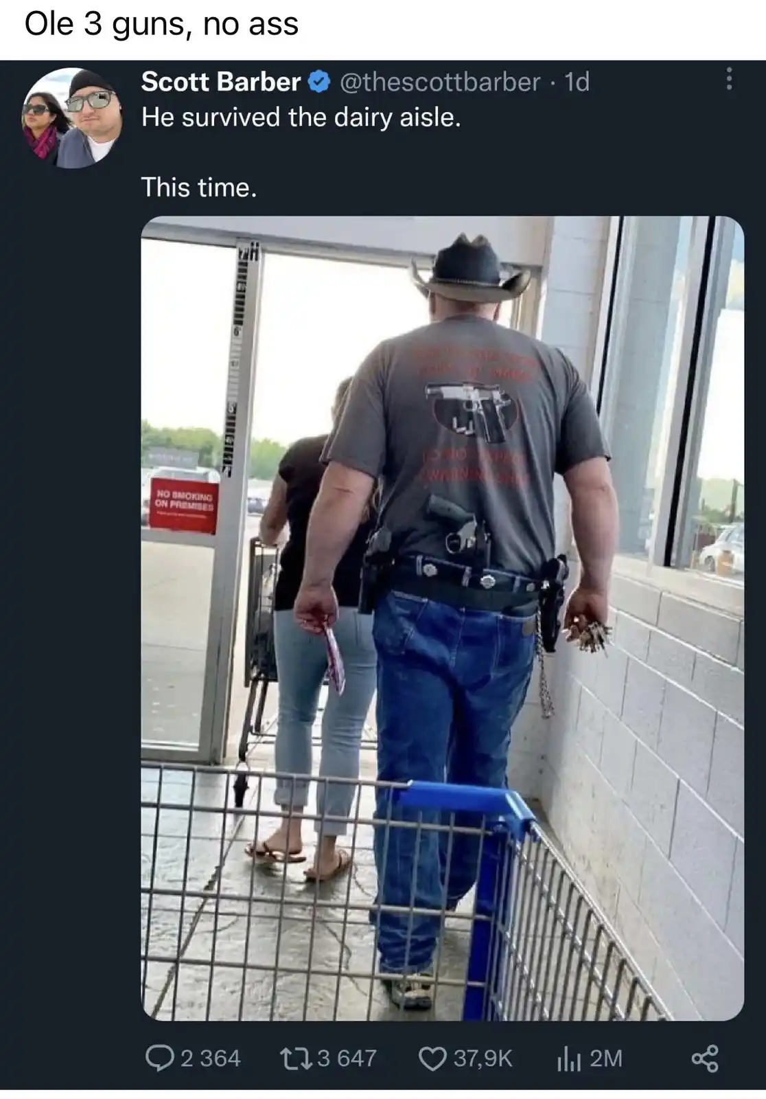 A man wearing a cowboy hat and a grey t-shirt with a gun graphic walks away from a store entrance, pushing a shopping cart…