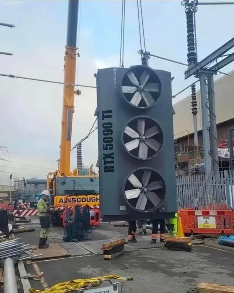 A large industrial crane lifts a massive, dark gray, vertically oriented object with three large circular fan-like…