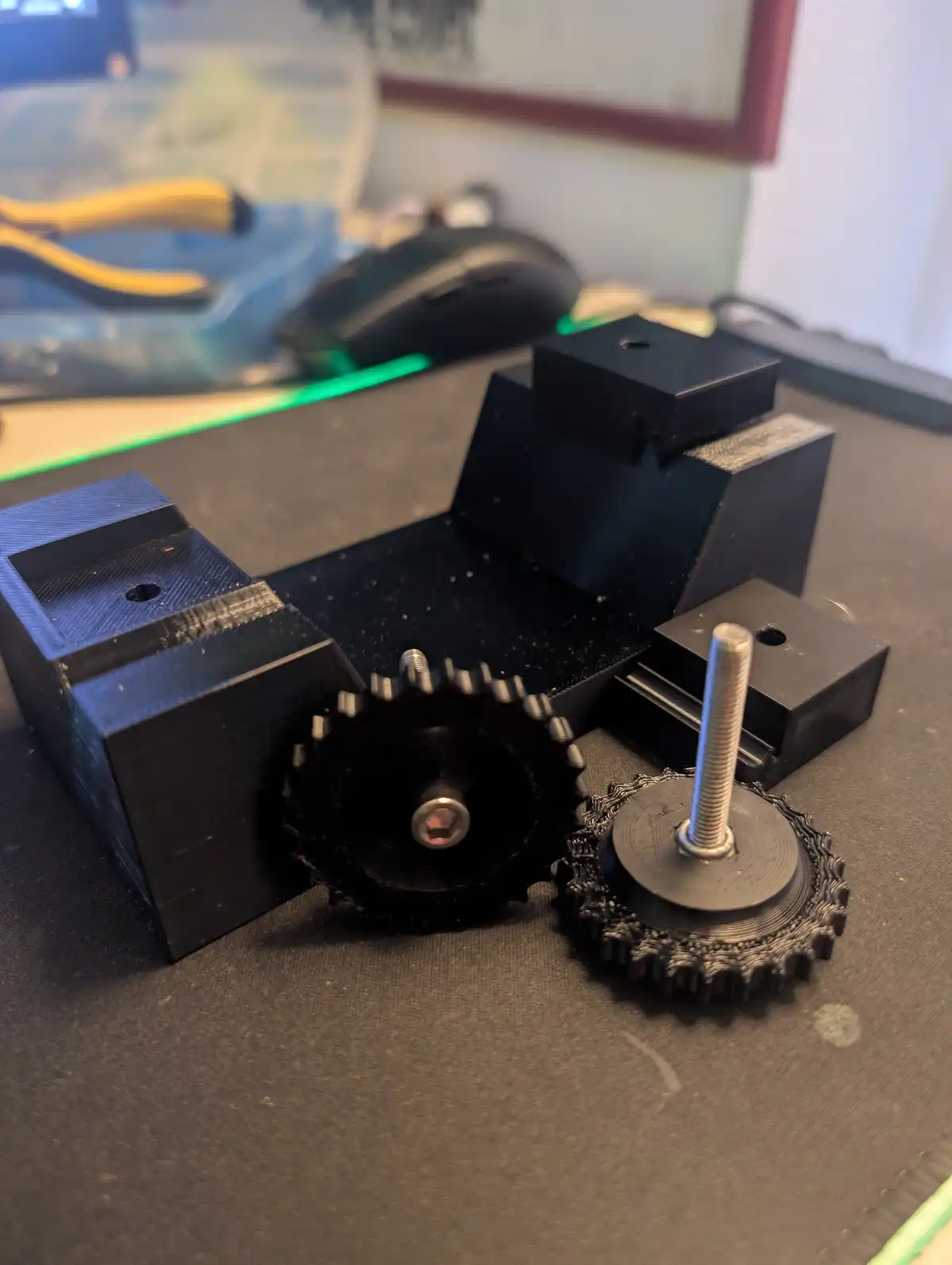 A close-up photo shows a homemade mechanical gear system made of 3d-printed black plastic parts, including two interlocking…