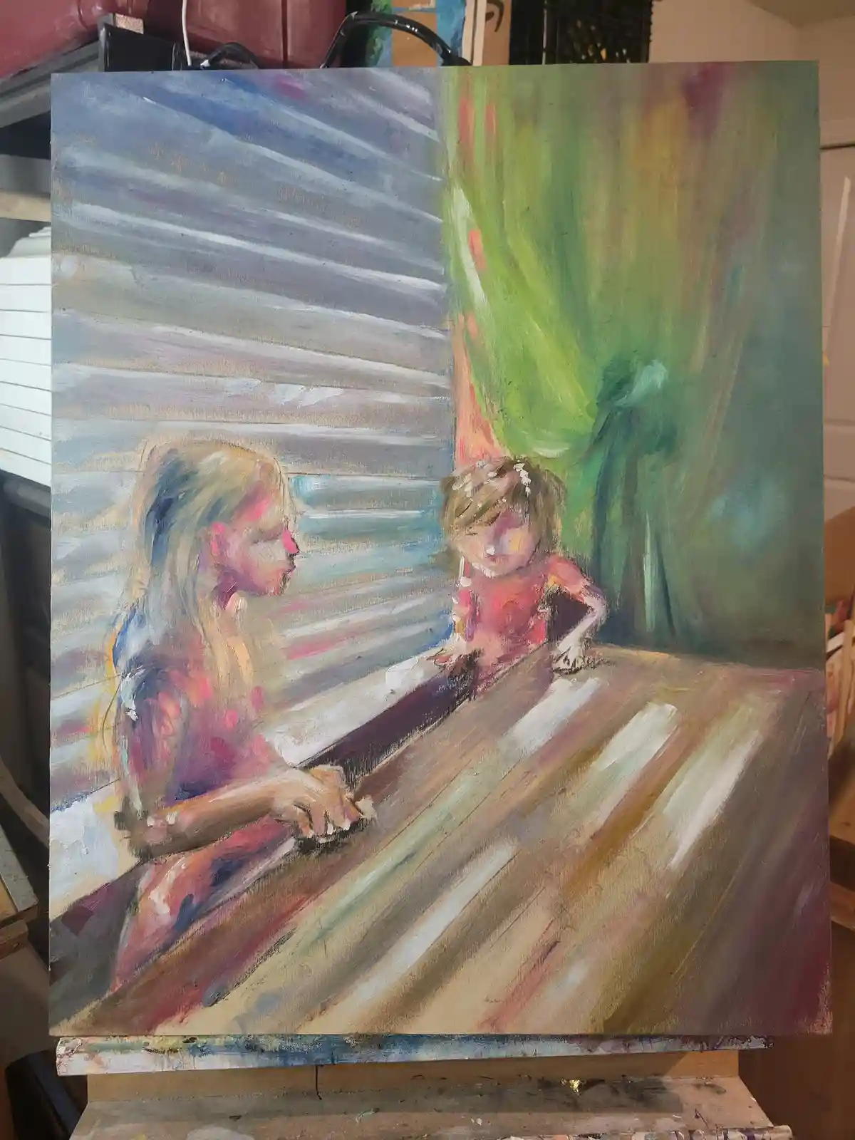 A painting depicts two young girls sitting at a table, one with long blonde hair and the other with short brown hair, both…