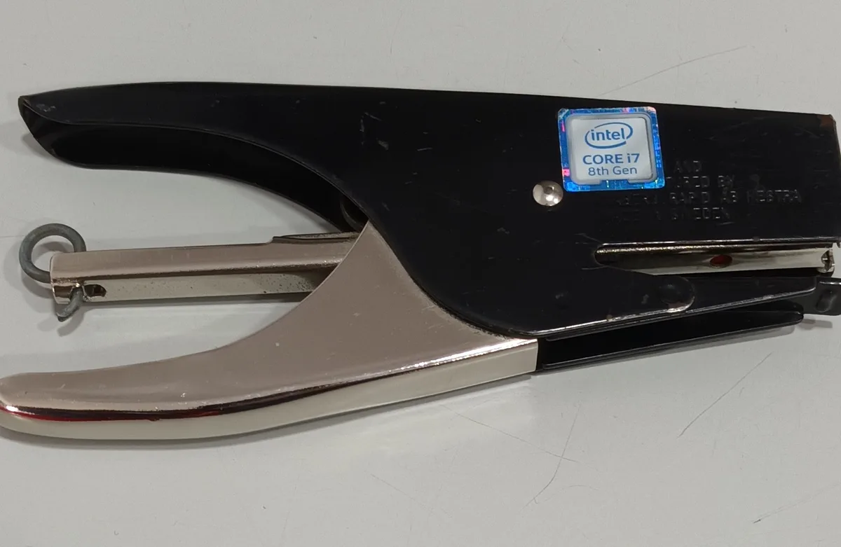 A black and silver stapler has an Intel Core i7 8th Gen CPU sticker affixed to its top surface, humorously implying the…