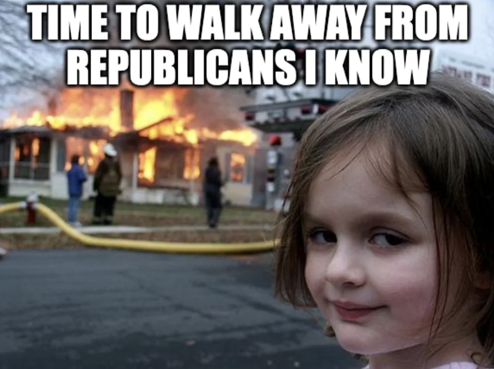 A young girl with a smug, self-satisfied expression looks at the camera while a house behind her is engulfed in flames with…