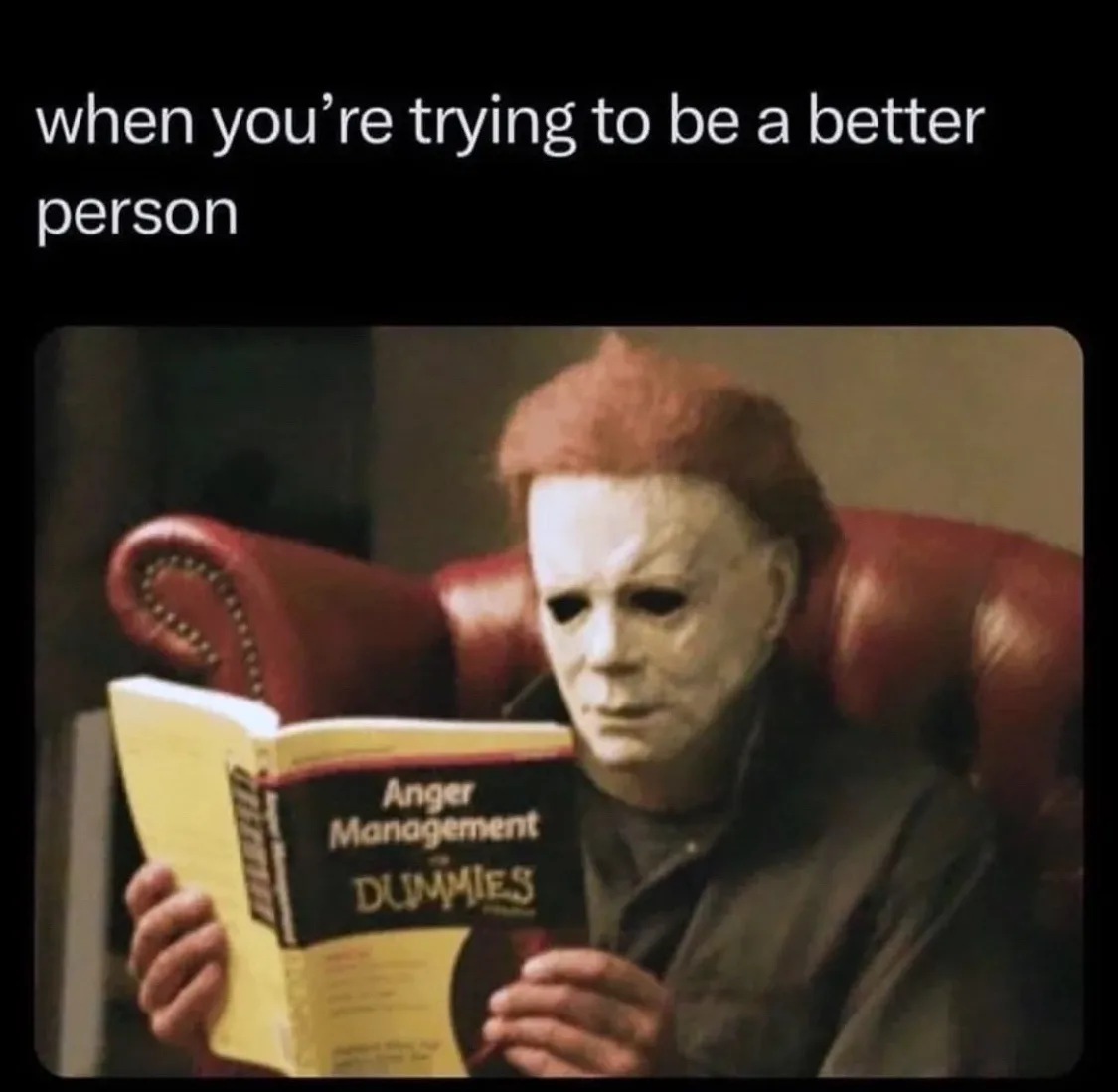 A person wearing a white Michael Myers mask sits in a red leather armchair, holding and reading a book titled 'Anger…