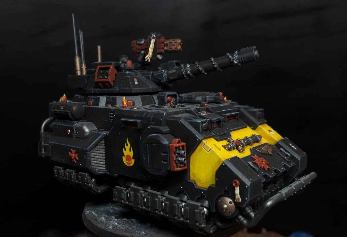 A highly detailed, painted miniature of a black and yellow armored tank with red and orange markings, including a flame…