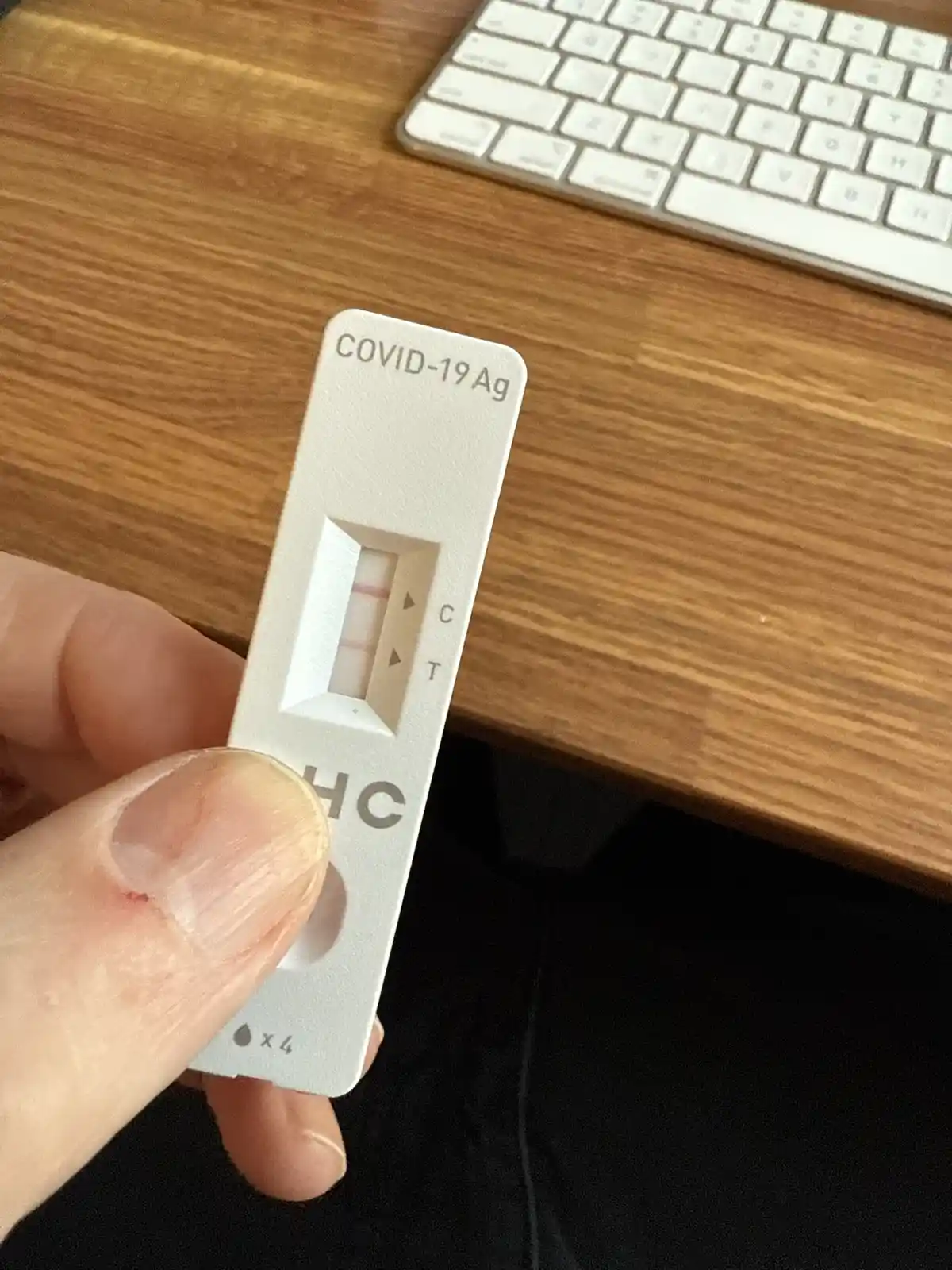 A hand holds a white COVID-19 antigen test device showing two pink lines, one at the 'C' control mark and one at the 'T'…