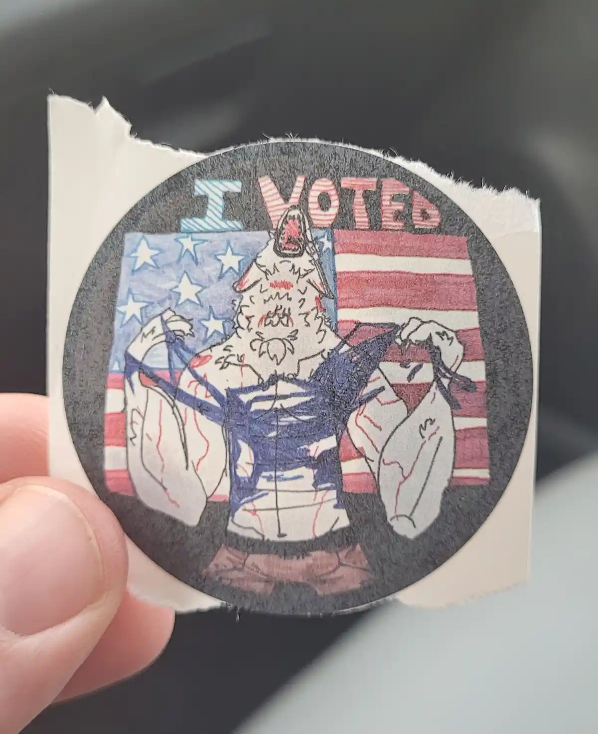 A hand holds a circular, hand-drawn sticker featuring a muscular, anthropomorphic wolf with a patriotic American flag…