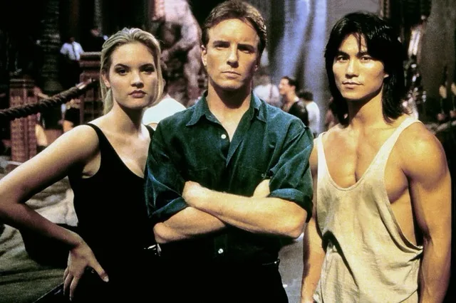 Three actors from the movie 'The Mummy' stand side-by-side with serious expressions. The central male figure has his arms…