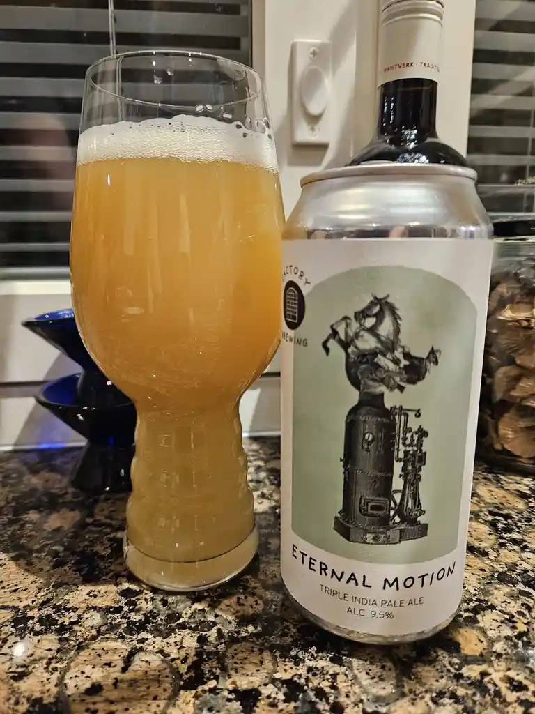 A beer can labeled 'Eternal Motion Triple India Pale Ale' sits next to a glass filled with amber beer and white foam, both…