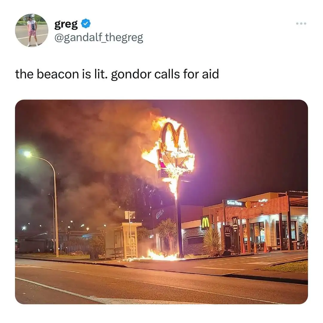 A nighttime photo shows a McDonald's restaurant with its iconic golden arches sign on a tall pole engulfed in flames and…