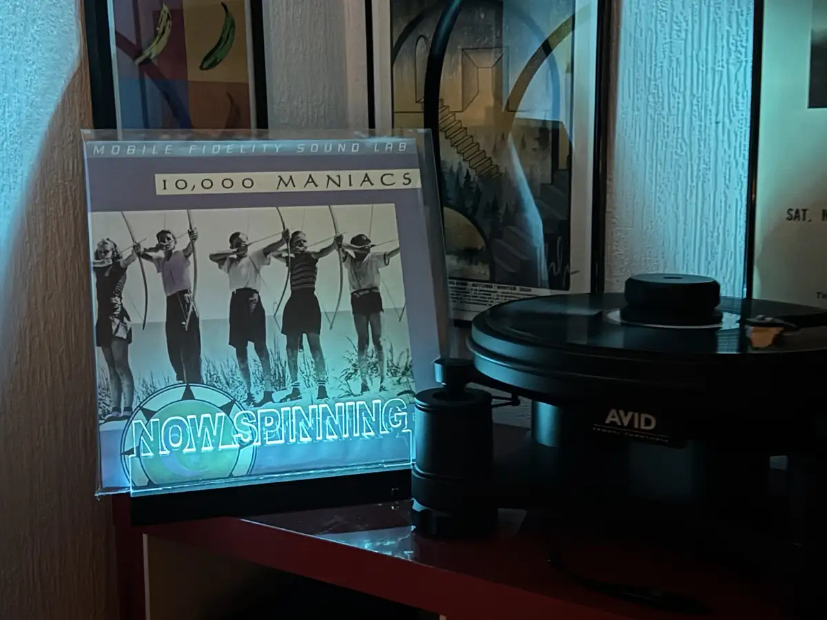 A vinyl record player sits next to a glowing album cover for '10,000 Maniacs' by Mobile Fidelity Sound Lab, which displays a…
