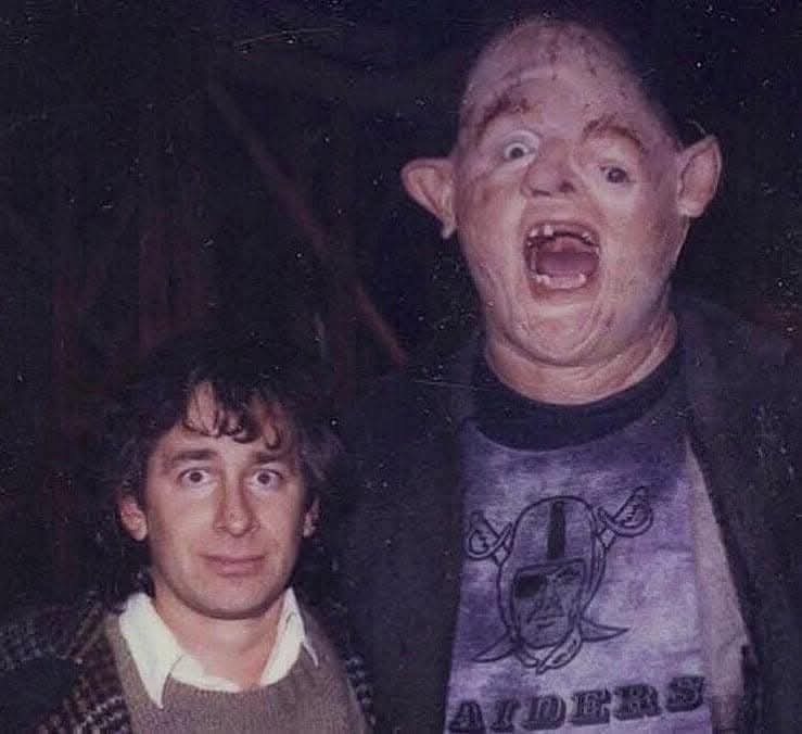 A grainy, low-light photo shows two men. The man on the right wears a Raiders t-shirt and has a grotesque, painted-up face…