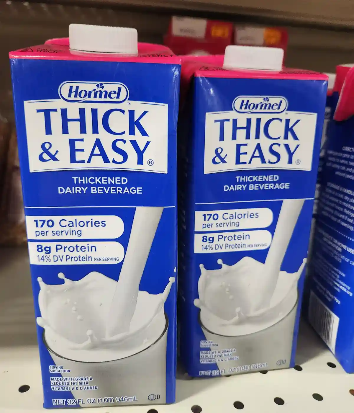 Two blue and pink Hormel Thick & Easy thickened dairy beverage cartons sit side-by-side on a store shelf, their labels…