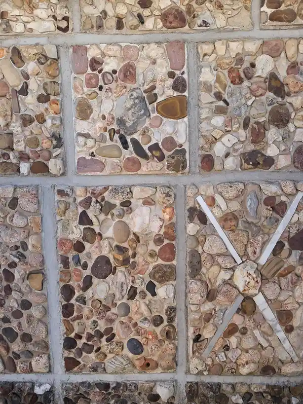 a close-up of a stone-paved walkway where one square panel has four white sticks arranged to form the letter 'x' over the…