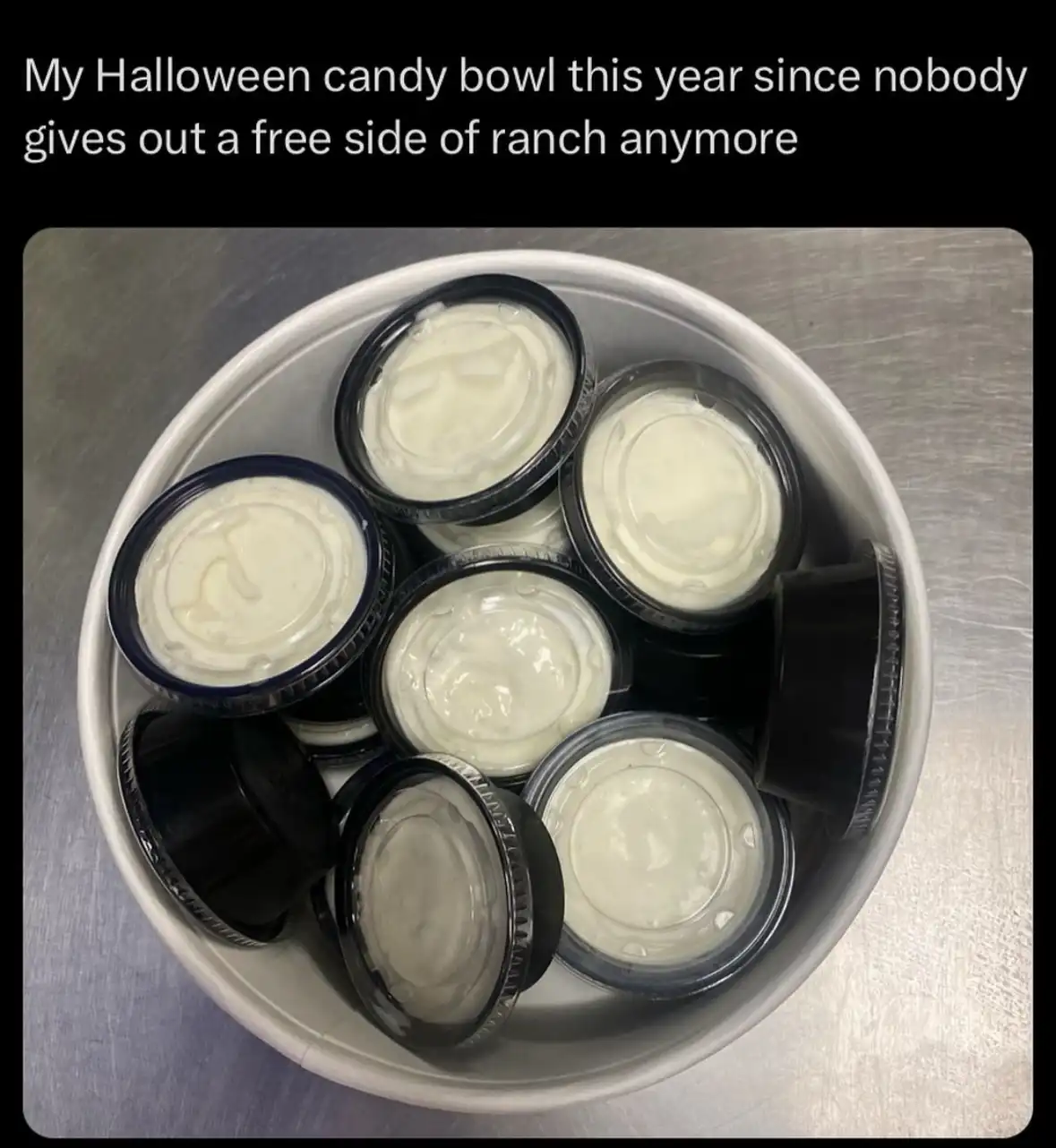 A white bowl filled with small, clear plastic cups containing creamy white ranch dressing, sitting on a stainless steel…