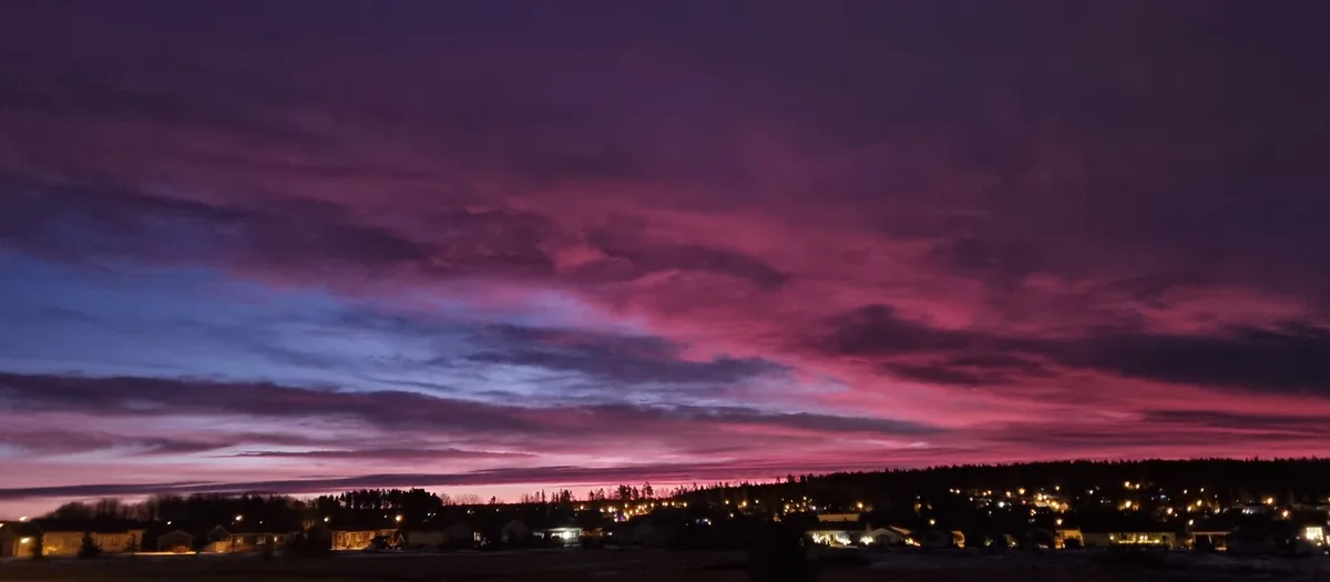 A wide-angle photo captures a dramatic twilight sky over a suburban neighborhood, with vibrant pink and purple clouds…