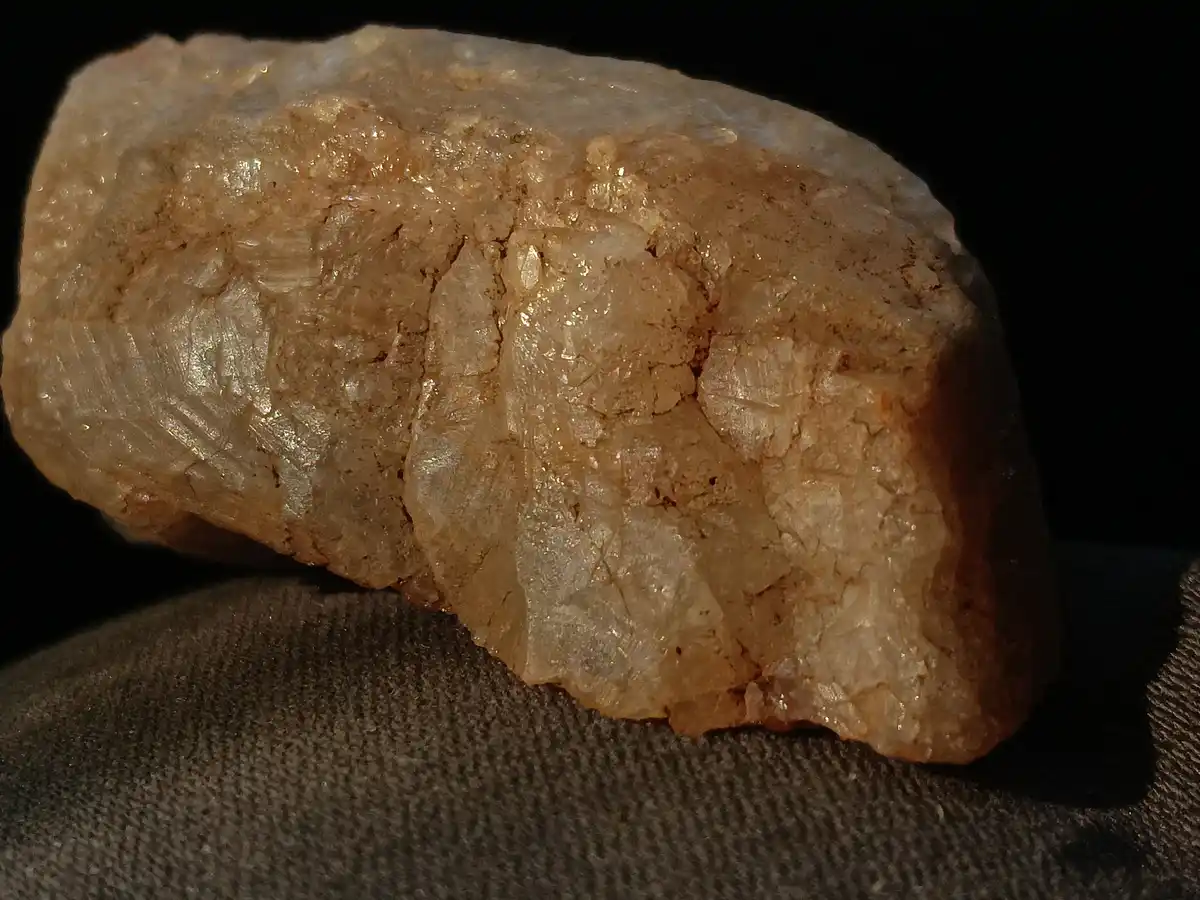 A close-up photograph shows a rough, translucent, beige-colored mineral specimen with visible crystalline textures and…