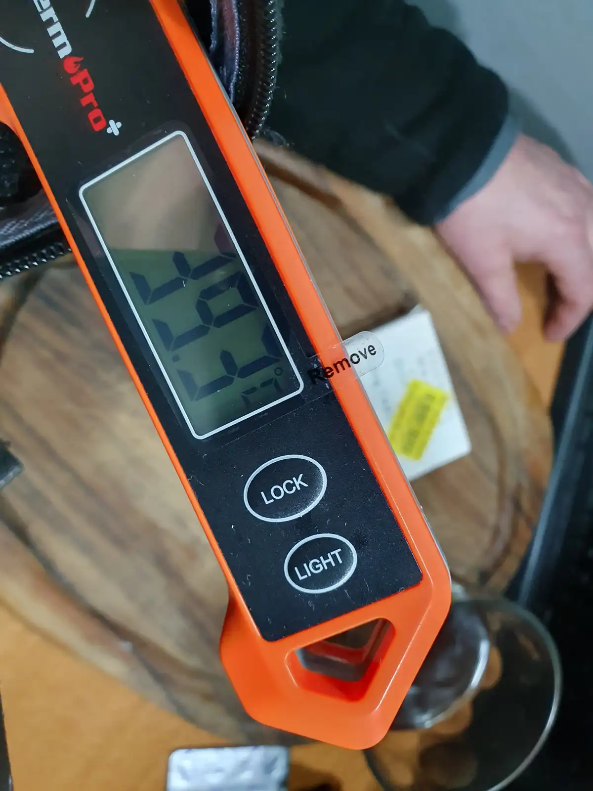 A close-up of an orange and black digital thermometer showing a reading of 46.5 degrees, with a small sticker labeled…