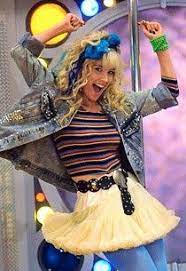 A young woman with blonde curly hair, wearing a denim jacket, striped shirt, and a yellow tutu, is captured mid-dance with…