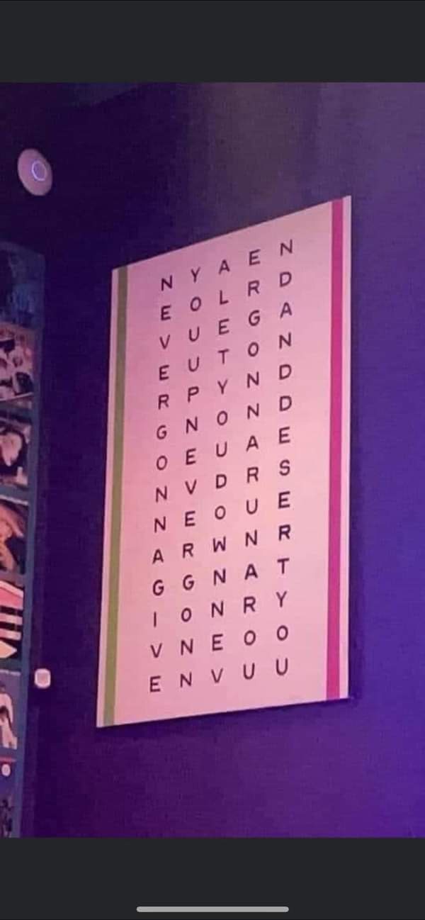 A pink wall-mounted sign with a grid of letters arranged in rows, resembling a word search puzzle, under purple ambient…