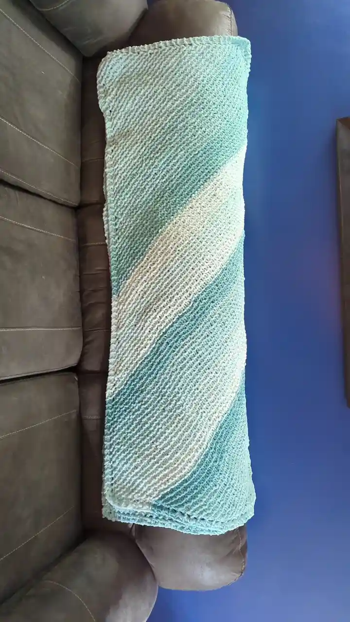 A hand-knitted blanket with diagonal stripes of light blue and off-white is draped over the back of a brown leather couch…