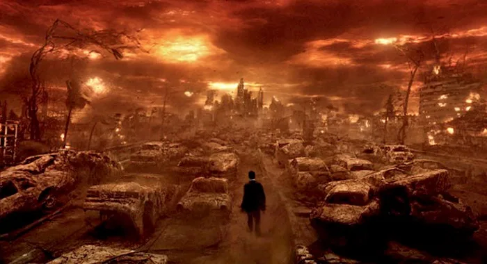 A lone figure walks through a desolate, post-apocalyptic wasteland filled with overturned and ruined cars under a fiery…