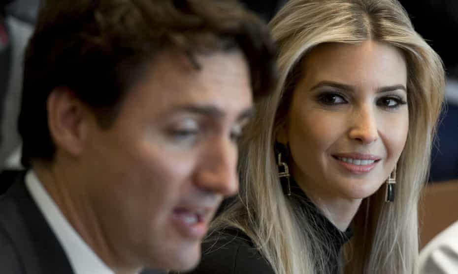 A photo shows a man in a suit speaking while out of focus, with a woman with blonde hair and earrings smiling directly at…