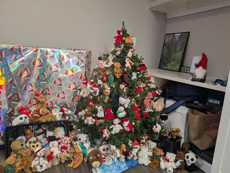 A Christmas tree is densely decorated with hundreds of Ty Beanie Babies plush toys, with many more piled in a crate and on…