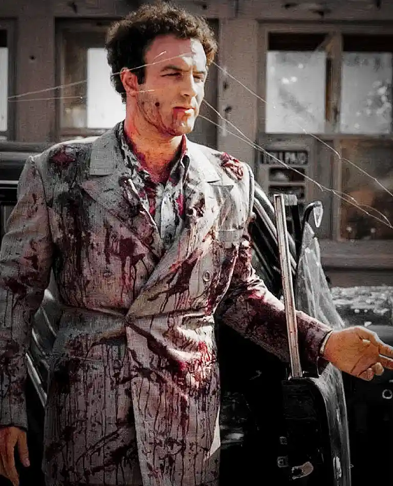 A man in a blood-splattered suit stands in front of a car, looking weary and injured, with a shattered glass effect…