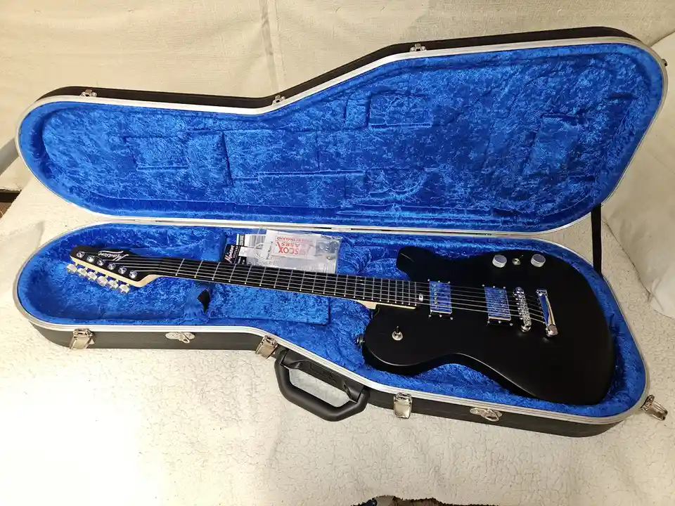 A black electric guitar with a light-colored headstock and blue pickguard rests inside an open, hard-shell case lined with…