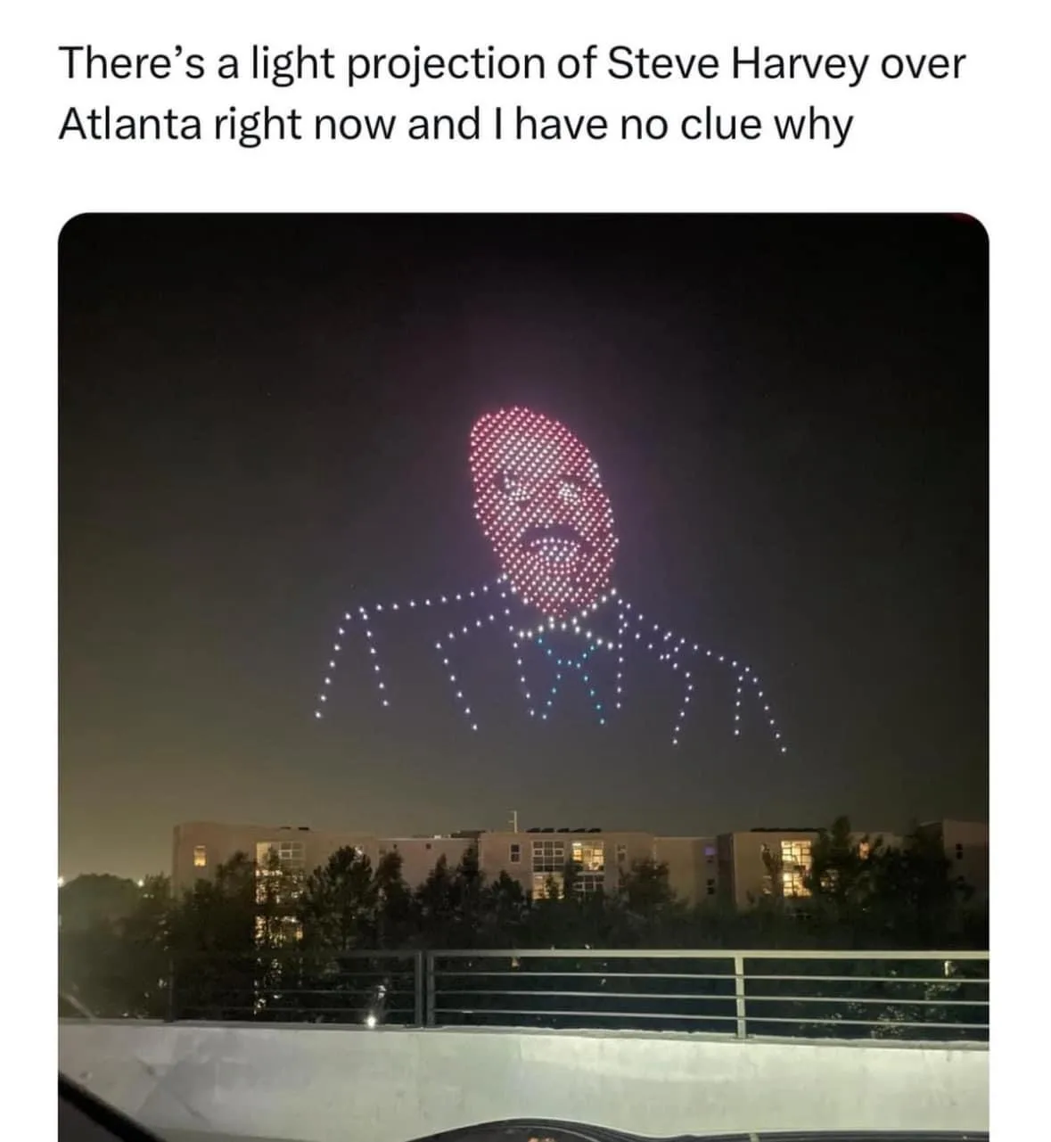 A nighttime photo taken from a car shows a large, pixelated projection of comedian Steve Harvey's face and upper torso…