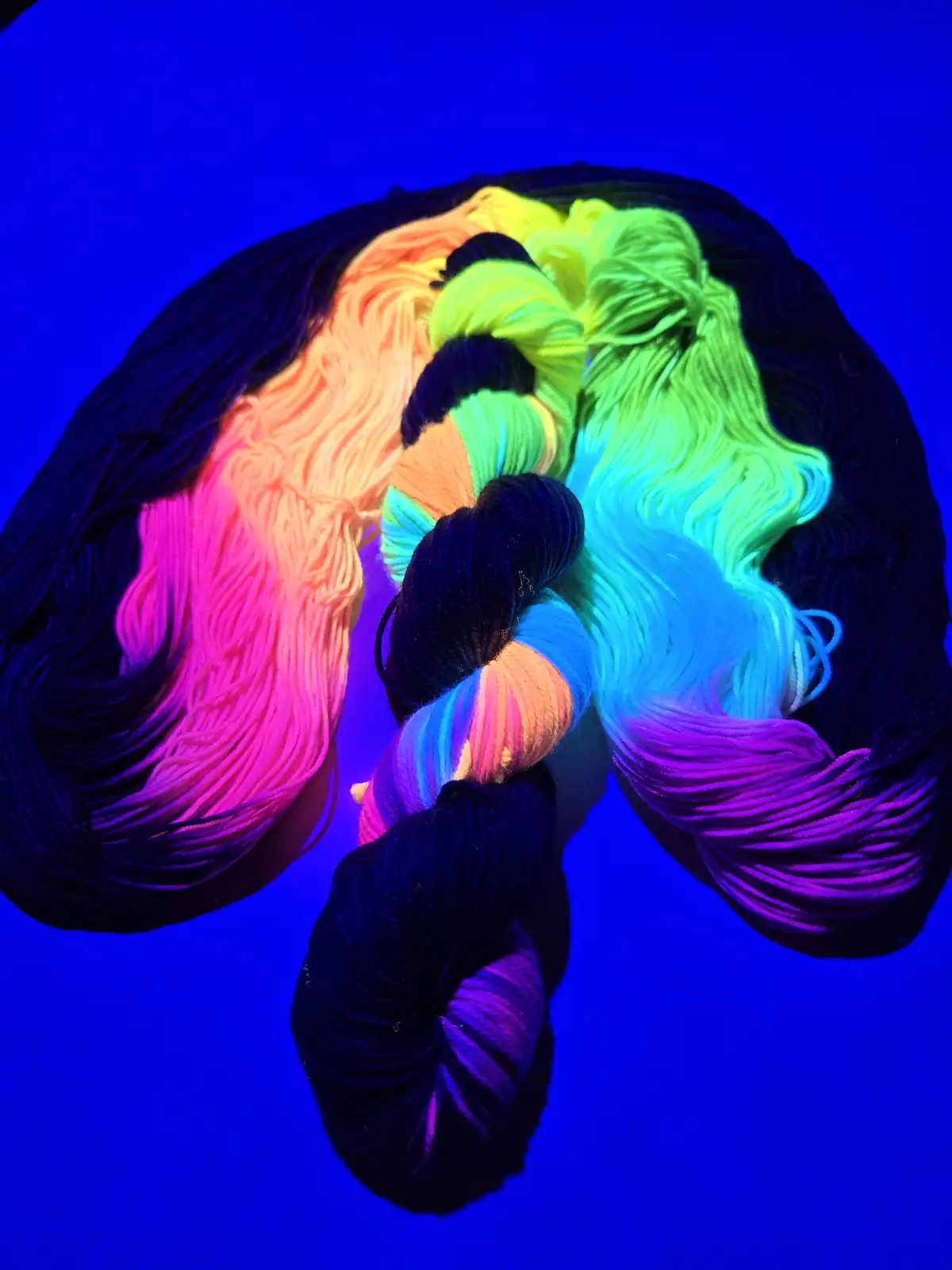 A close-up shot of several skeins of yarn arranged to resemble a human head with long hair, glowing with vibrant neon colors…