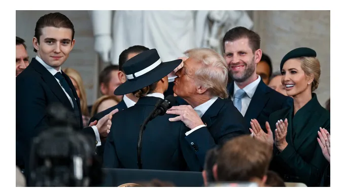 A man in a dark suit and black hat is being kissed on the forehead by former president Donald Trump, who is also in a dark…