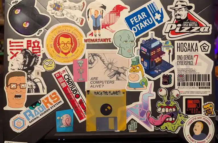 A black surface covered in a dense collage of colorful stickers featuring anime, cartoons, video games, and pop culture…