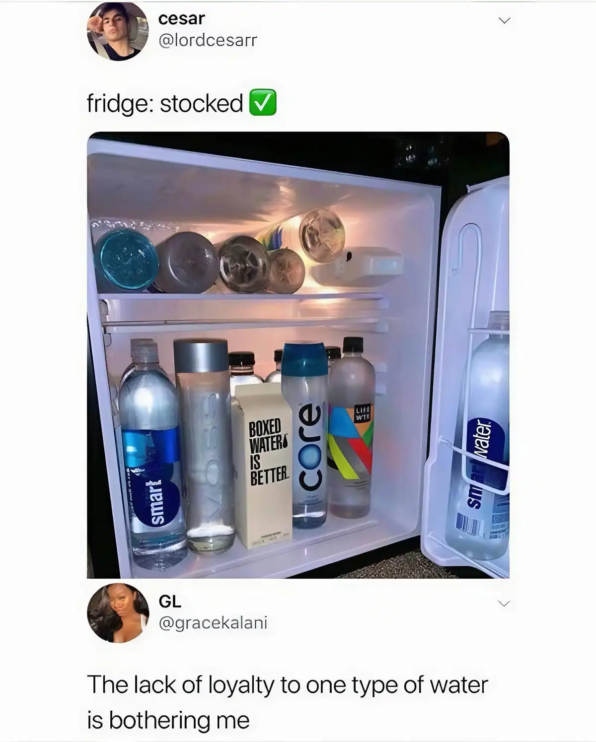 An open mini-fridge is filled with various brands of bottled and boxed water, including Smartwater, Voss, Core, and a box…