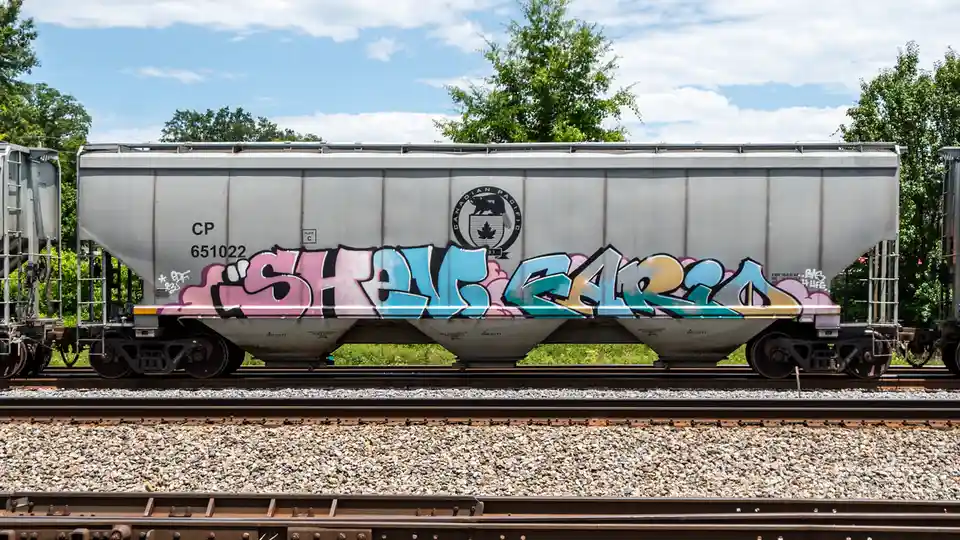 A silver Canadian Pacific freight train car, marked with the number 651022, is covered in colorful graffiti that spells out…