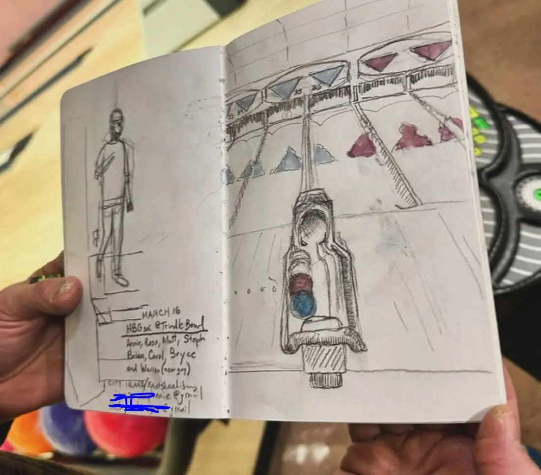 A hand holds an open sketchbook showing two drawings: a simple sketch of a person on the left page, and a detailed sketch of…