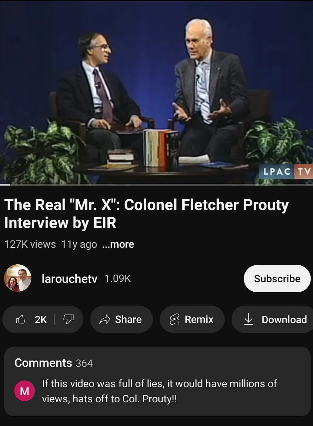 A screenshot of a YouTube video thumbnail showing two men in suits seated at a table with books and plants, overlaid with…